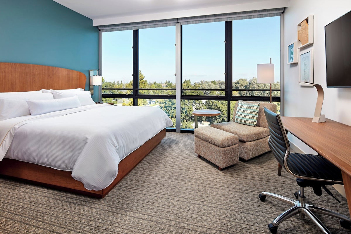 A hotel room with a large bed, a desk, a chair, and a view of the outdoors.