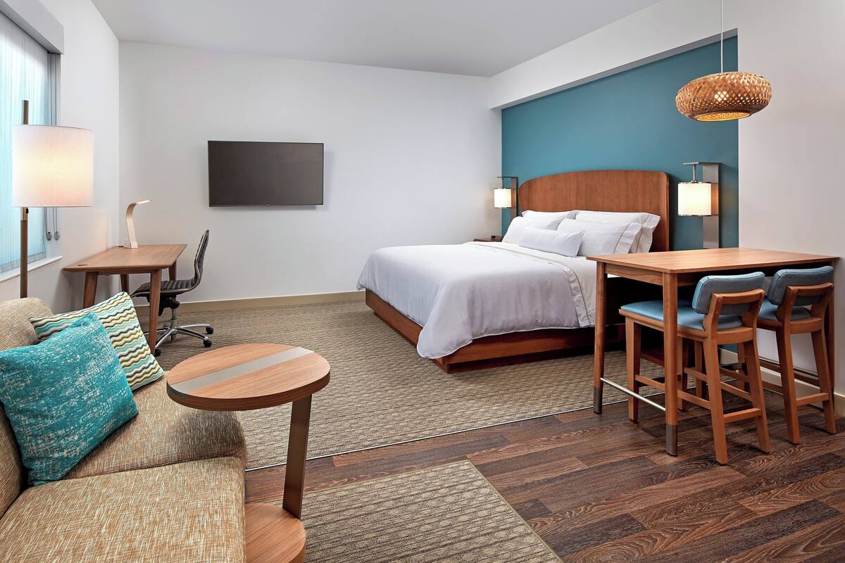 A modern hotel room with a bed, a desk, a chair, a sofa, and a TV.
