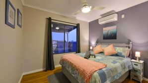 A bedroom with a bed, bedside tables, a ceiling fan, a window with curtains, and an air conditioning unit.