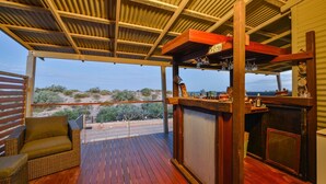 A covered outdoor seating area with a wooden deck, a bar with a view, and a wicker sofa.