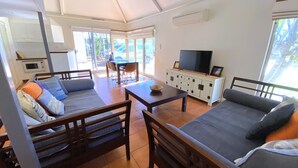 A cozy living area with a sofa, a dining table, and a TV. There is a kitchen area with a microwave and cabinets. - Osprey Holiday Village Unit  112 - 3 Bedroom Fully Self-Contained Holiday Accommodation (EXMOUTH)