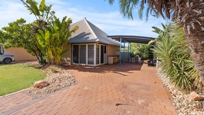 A house with a covered patio, a car parked in the driveway, and a garden with various plants. - Osprey Holiday Village Unit  112 - 3 Bedroom Fully Self-Contained Holiday Accommodation (EXMOUTH)