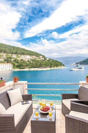 A balcony with wicker furniture, a table with breakfast items, and a view of a coastal town and sea. - Holiday Home Puteus (Selca)