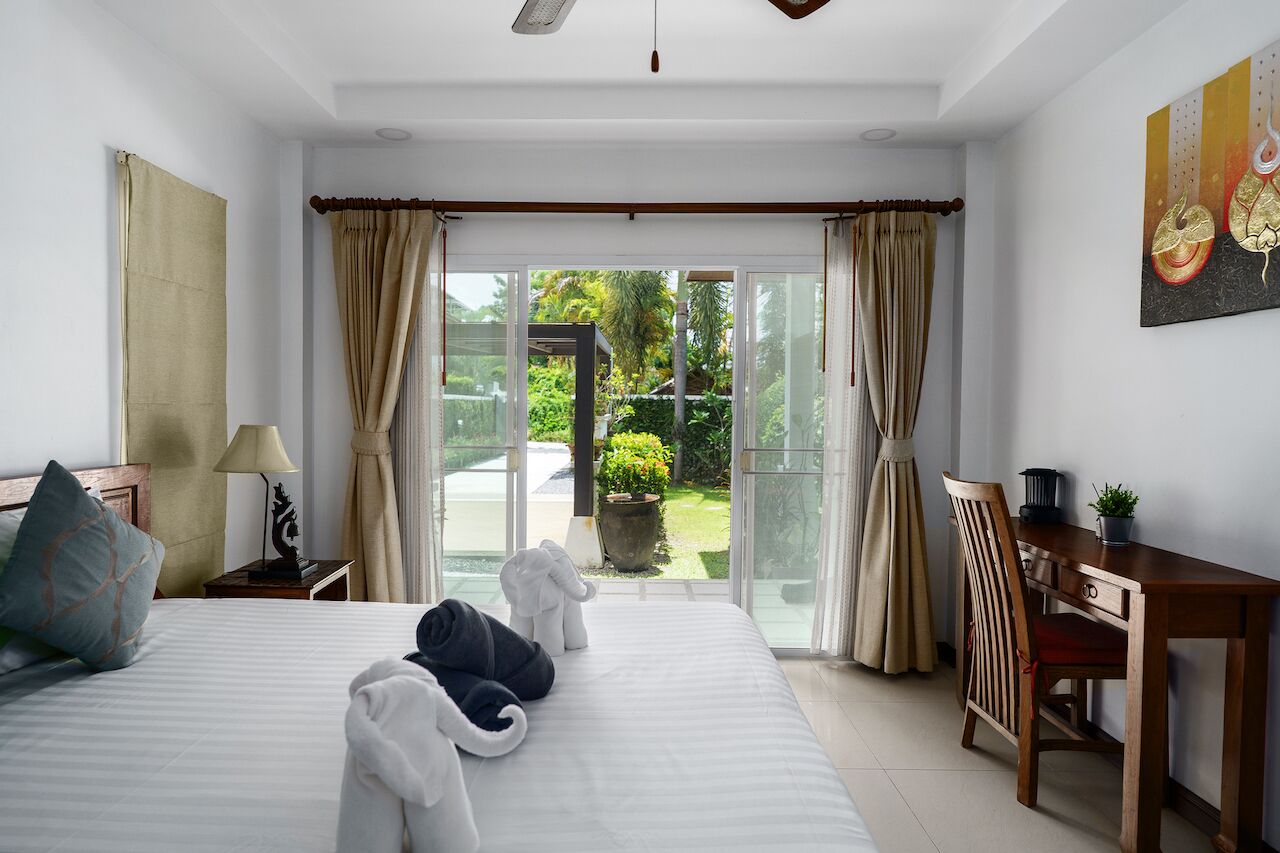 Une chambre d’hôtel équipée d’un lit, d’un bureau, d’une chaise et offrant une vue sur un jardin grâce à de grandes fenêtres.