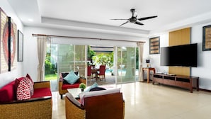 Una sala de estar moderna con mobiliario de mimbre, un televisor de pantalla plana y un ventanal corredero que da a un patio con zona de estar al aire libre.