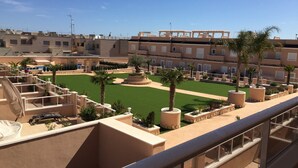 A rooftop terrace with a green lawn, palm trees, and a view of the surrounding buildings. - 3027 Vista Azul,close to the beach &  heated pool (Torre de la Horadada)