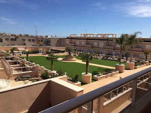 Una terraza en la azotea con césped verde, palmeras y vistas de los edificios circundantes.