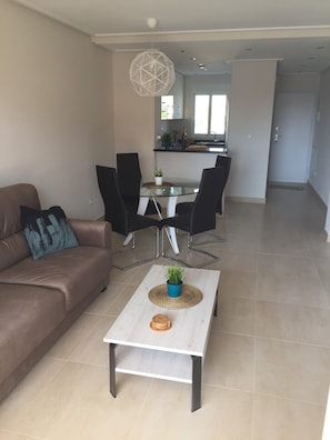Un salon moderne avec un canapé marron, une table basse en verre agrémentée d’une plante, et un coin repas avec une table en verre et des chaises noires.