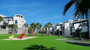 Un quartier résidentiel moderne doté d’une aire de jeux, de palmiers et de maisons contemporaines.