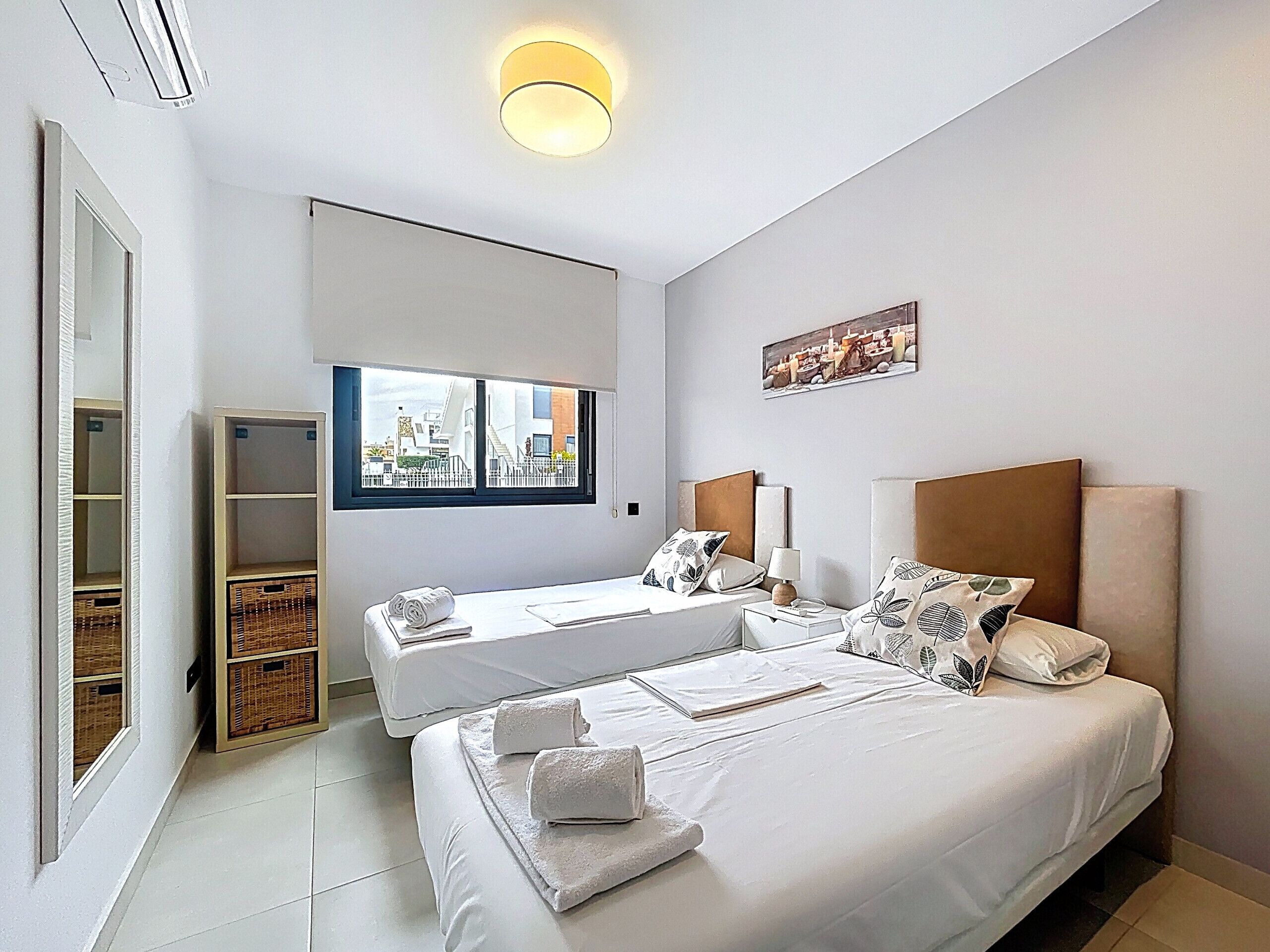Ein modernes Hotelzimmer mit einem großen Bett, einem kleineren Bett, einem Fenster mit Blick auf die Stadt, einem Bild an der Wand und einer eingebauten Garderobe.