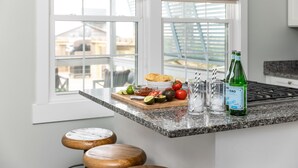 Eine Küche mit einer Granitabdeckung, einem Fenster mit Blick auf Gebäude, einer Gin-Flasche und einem Schneidebrett mit Gemüse.