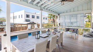 Eine überdachte Außenveranda mit Pool, Esstisch, Stühlen und Deckenventilator.