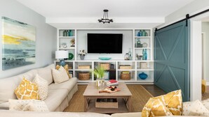 Ein Wohnzimmer mit einer Couch, einem Couchtisch und einem Fernseher. Regale mit Dekoration und eine Schiebetür sind ebenfalls vorhanden.