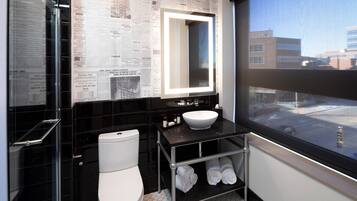 Un baño moderno con pared de azulejos negros, un inodoro blanco, un lavamanos con espejo y una ventana con vistas a edificios.