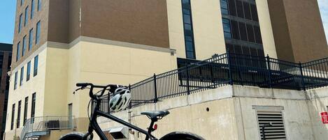 A bicycle parked in front of a building with a beige and brown facade, large windows, and a black metal fence.