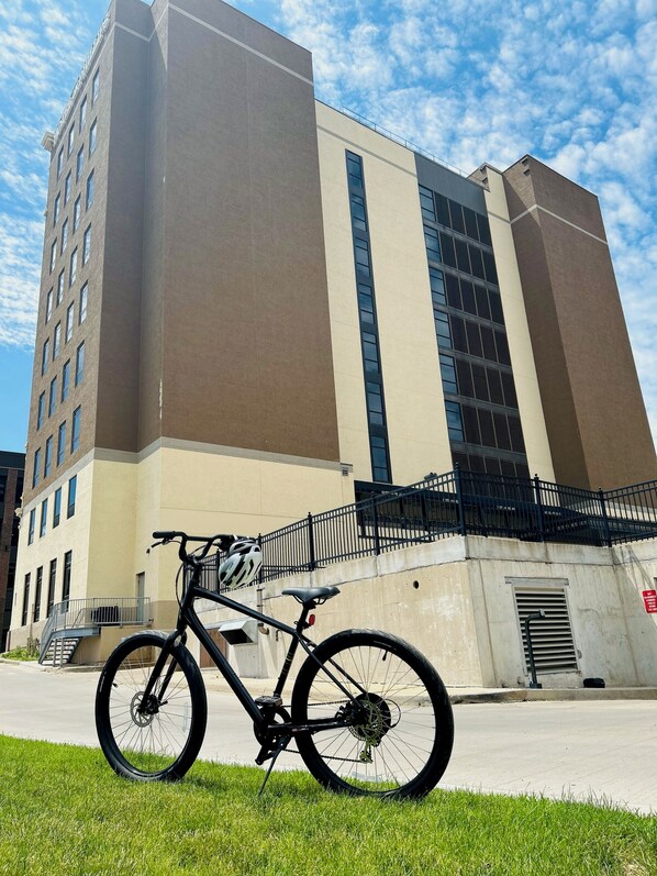 Una bicicleta estacionada frente a un edificio de fachada color beige y marrón, con ventanas grandes y una cerca de metal negro.
