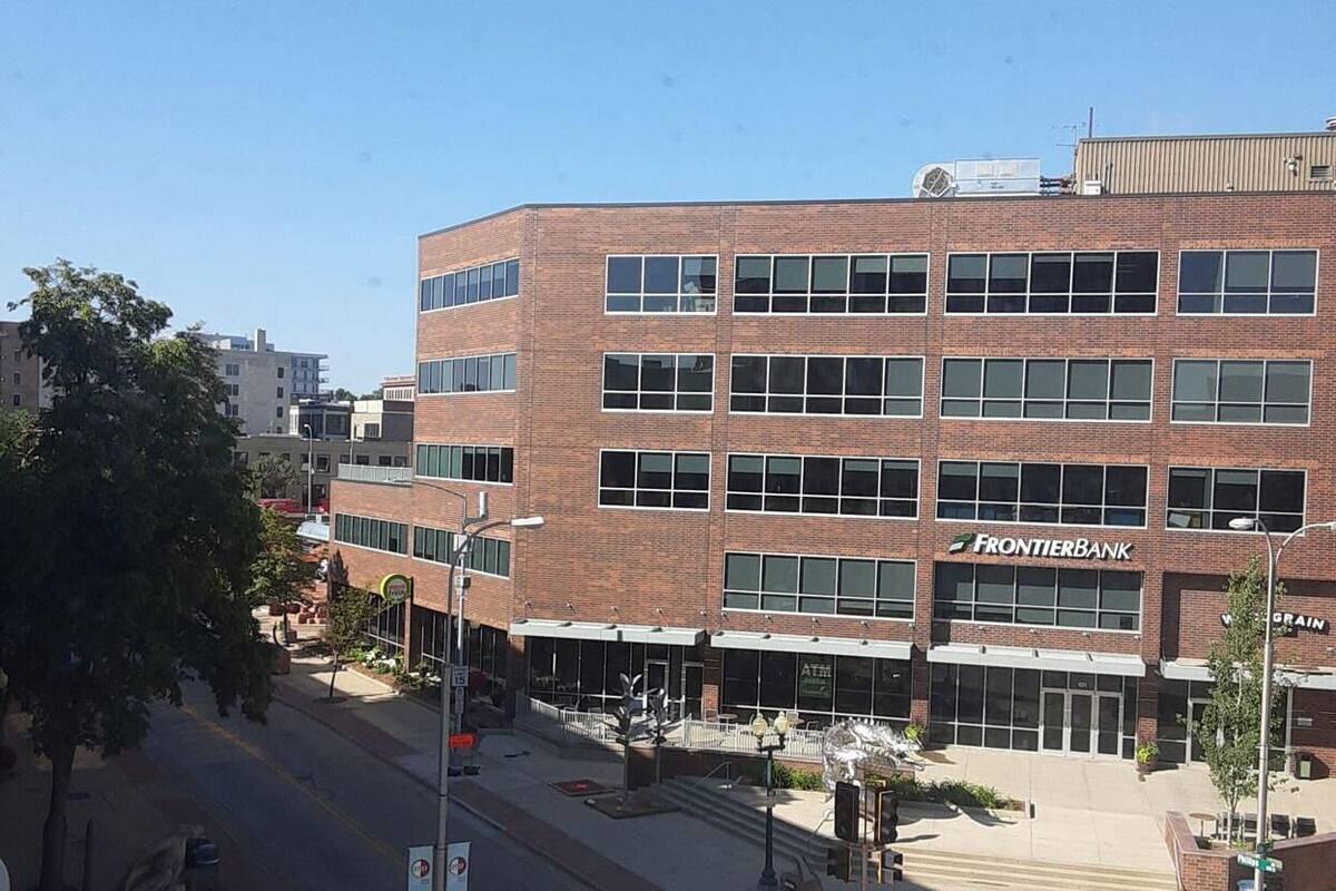 A multi-story building with a brick facade, a visible storefront with a sign, and a crosswalk in front.
