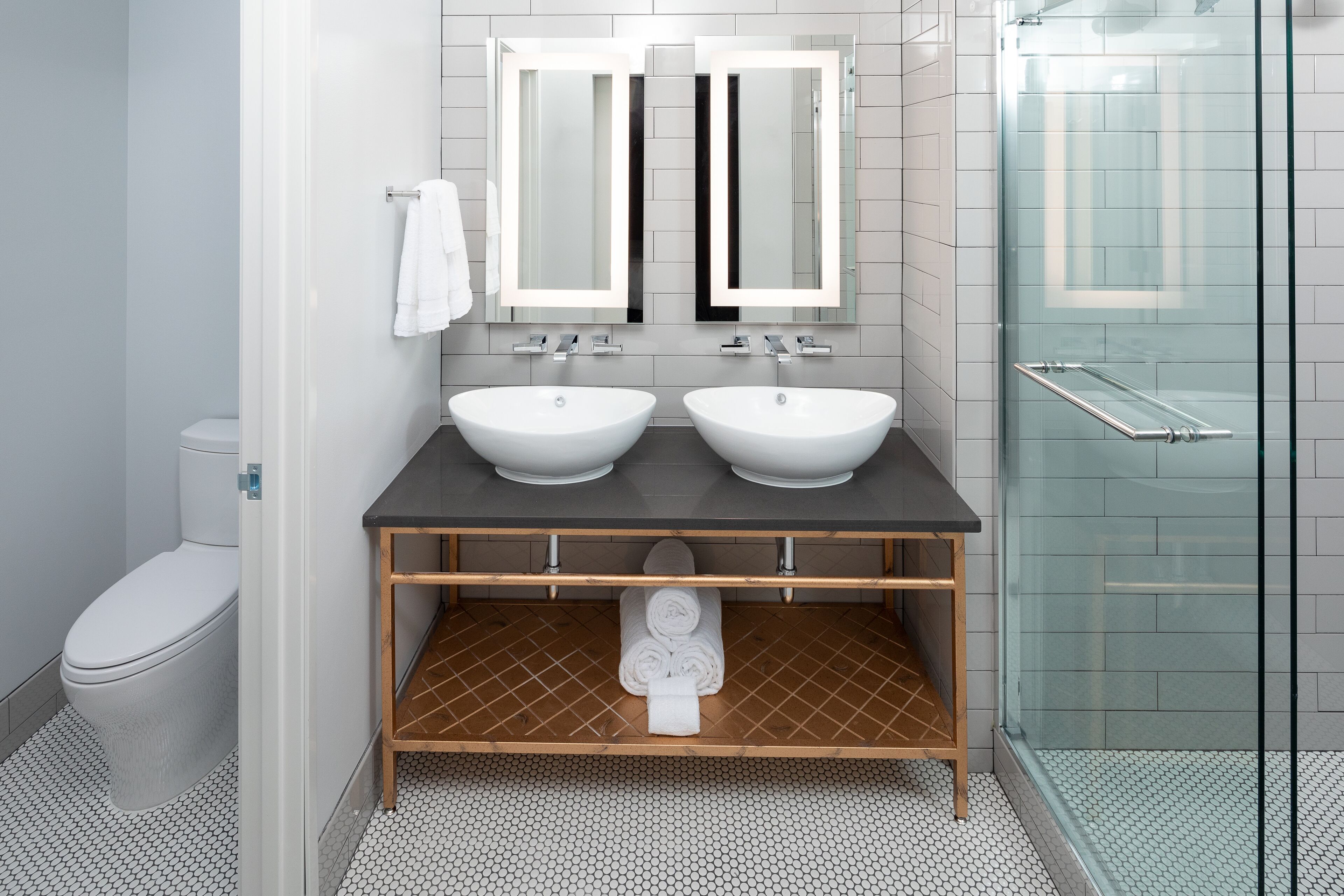 Un baño moderno con dos lavabos, un inodoro, ducha con puertas de vidrio y un mueble de tocador de madera.