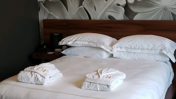 A neatly made bed with white linens and towels, a wooden headboard, and a wall with a large floral carving.