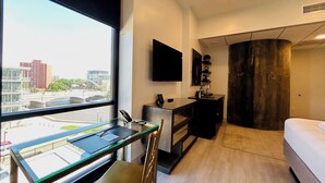 Una habitación de hotel moderna con escritorio, silla y cama. Cuenta con un ventanal con vistas a la ciudad, un televisor de pantalla plana y un armario de madera.