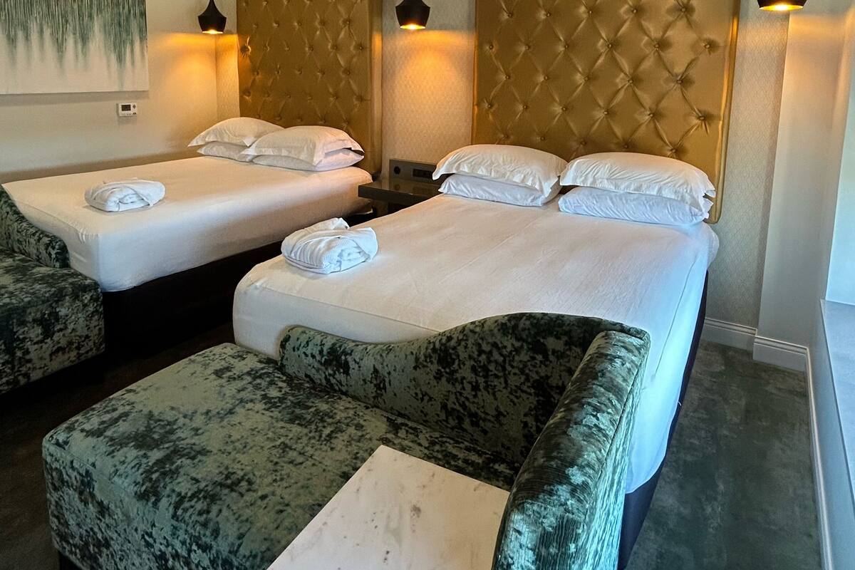 A hotel room with two beds, each with a tufted headboard, a small sofa, and a painting on the wall.