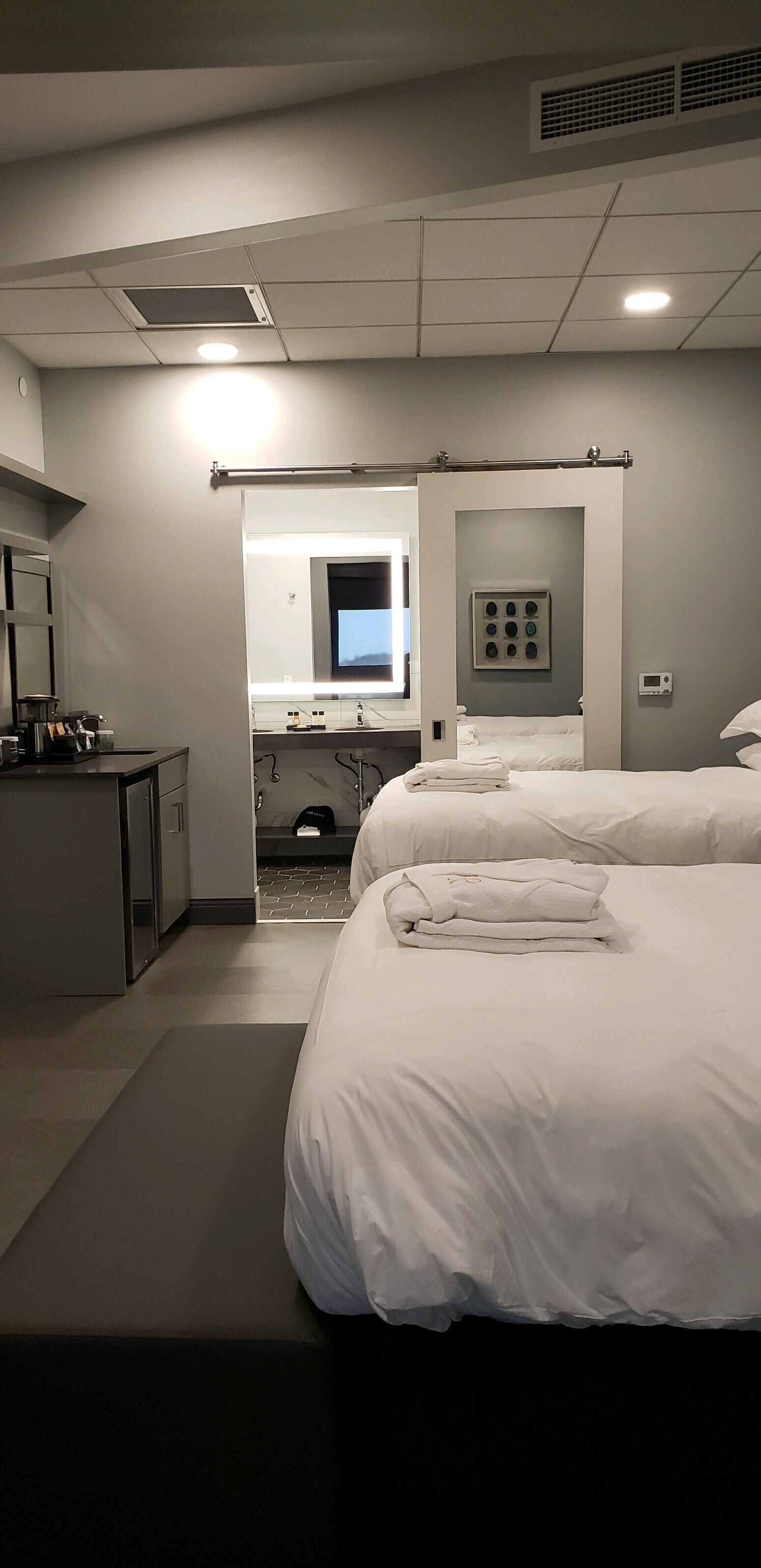 A hotel room with a bed, a desk, a mirror, and a bathroom visible through an open door.