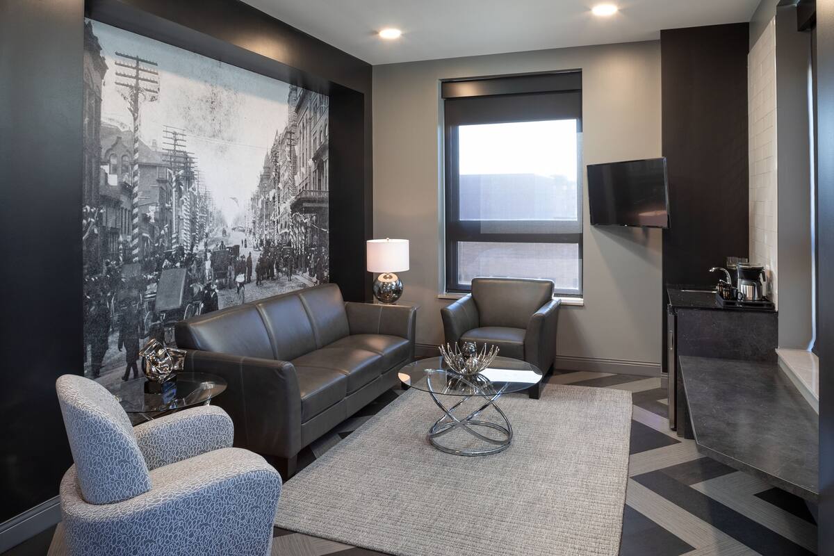 A modern living room with a large black and white photograph on the wall, a leather sofa, a glass coffee table, and a flat-screen TV mounted on the wall.