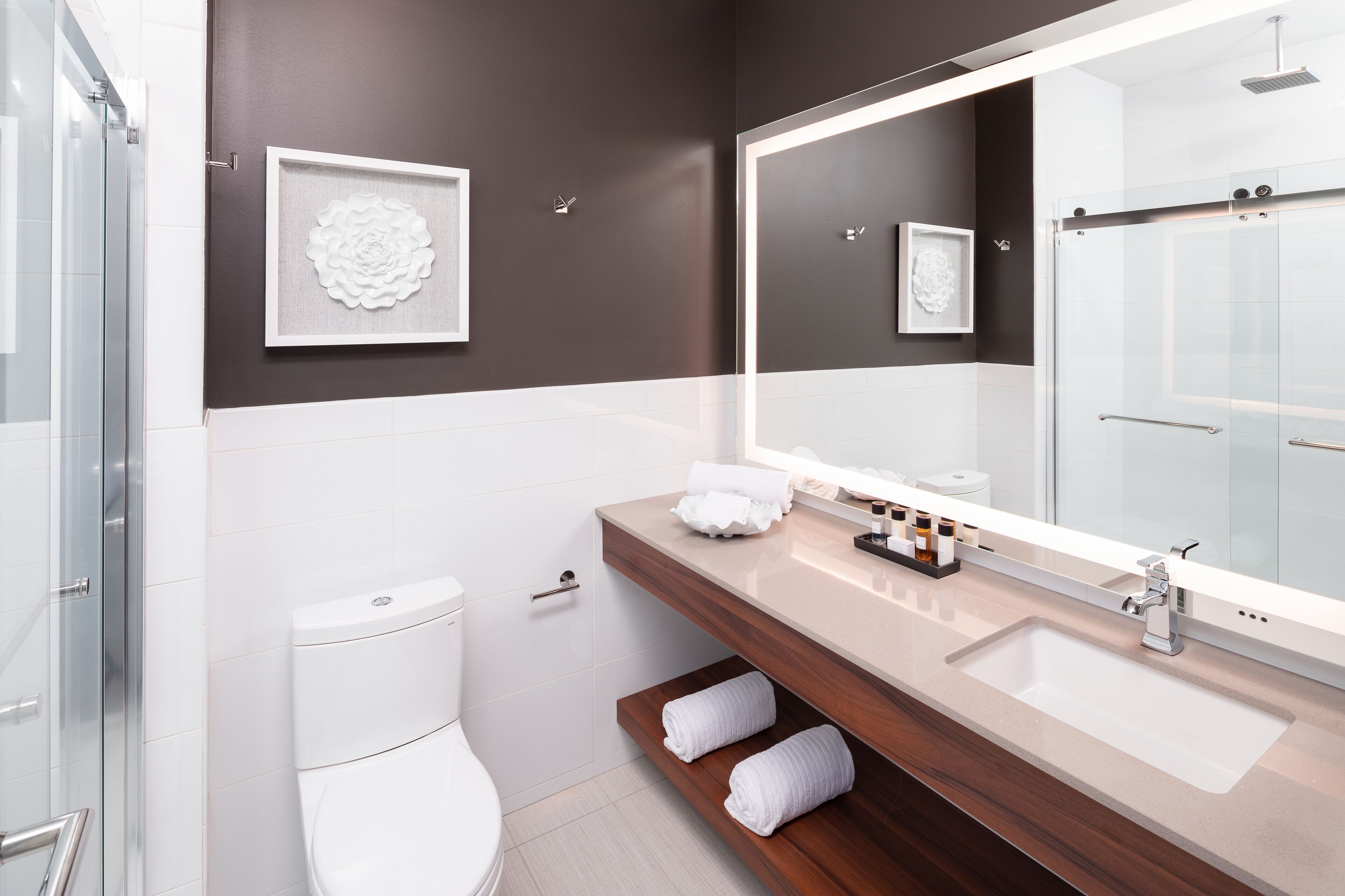 A modern bathroom with a large mirror, a sink, and a toilet.