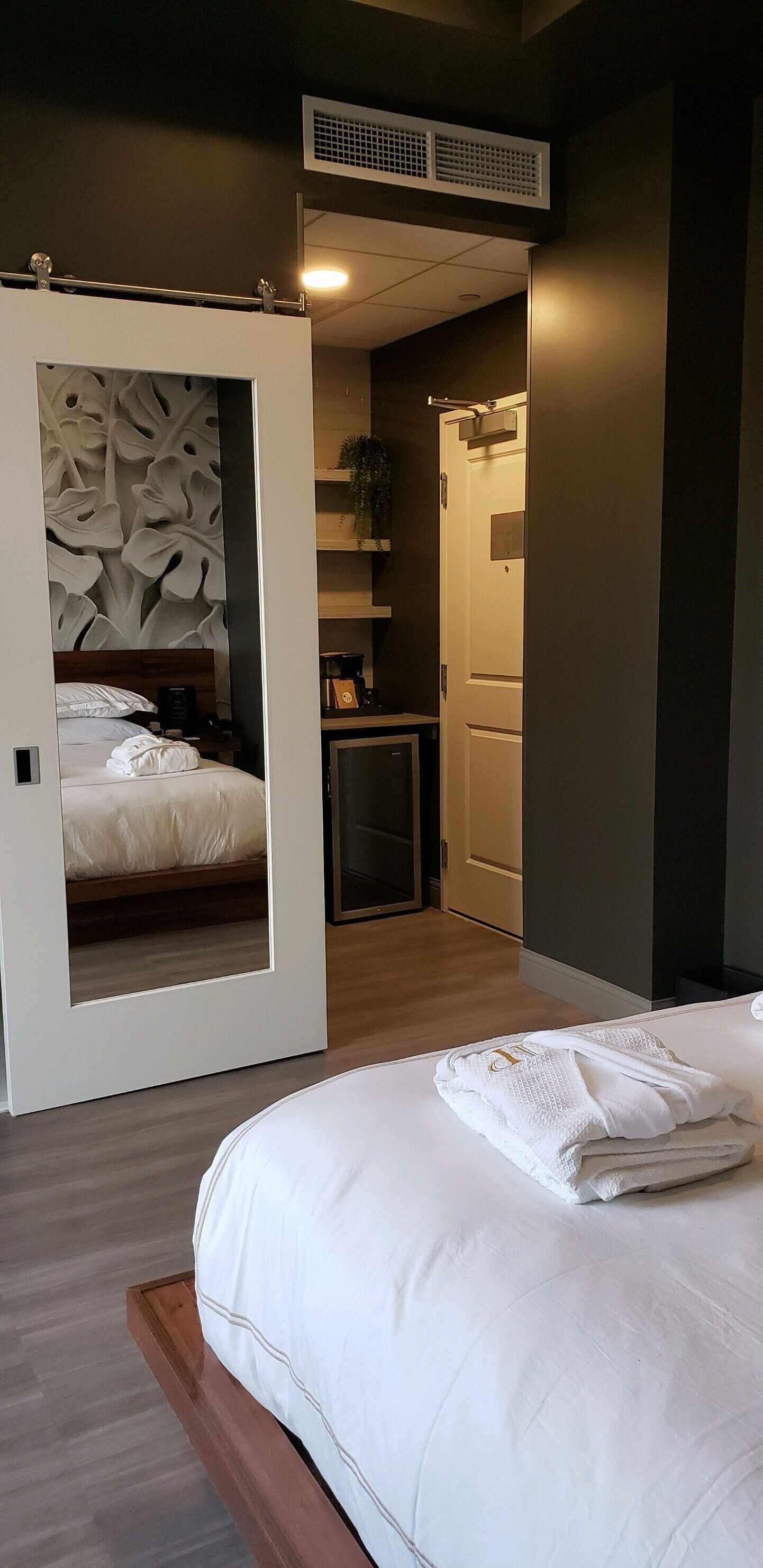 Una habitación de hotel moderna con una cama grande, un escritorio pequeño, un espejo y una puerta que da a un baño.