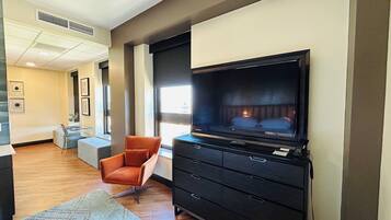 A hotel room with a large flat-screen TV, a comfortable orange chair, a small desk, and a patterned rug.