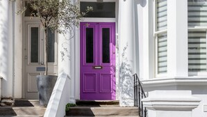 Un bâtiment doté d’une porte violette bien visible, de colonnes blanches et d’un escalier en pierre menant à l’entrée.