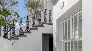 Un bâtiment blanc avec un escalier menant à une porte, une fenêtre avec des cadres blancs et une rambarde en métal.