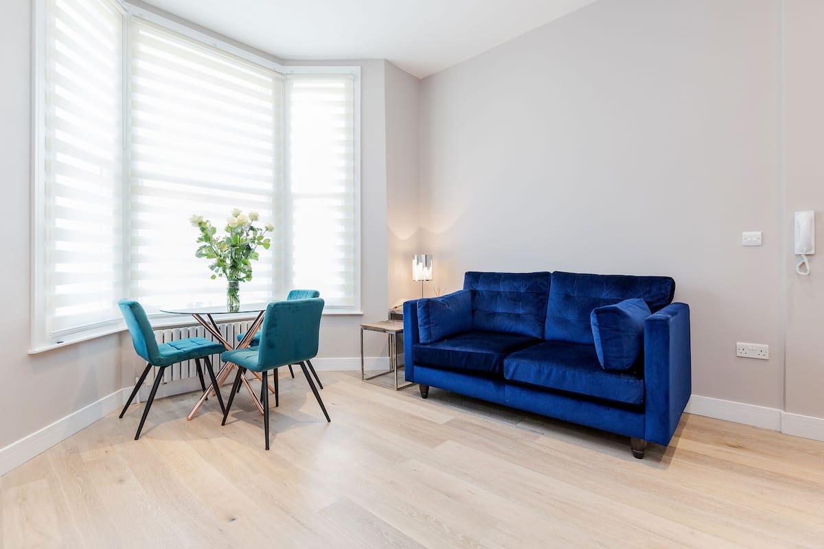 A modern living room with a blue sofa, teal chairs, a small table, and a vase of flowers.
