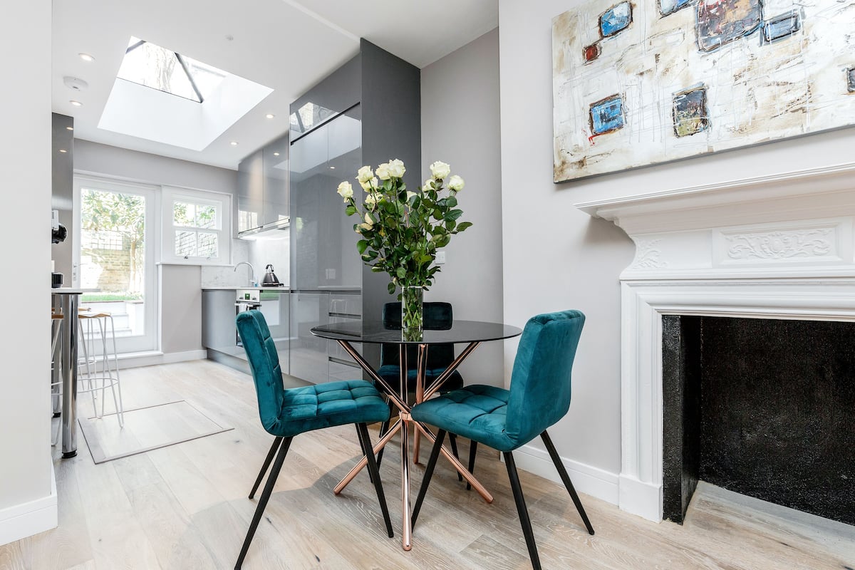 A modern kitchen with a glass door leading to a balcony, a dining area with a round table and teal chairs, and a fireplace.