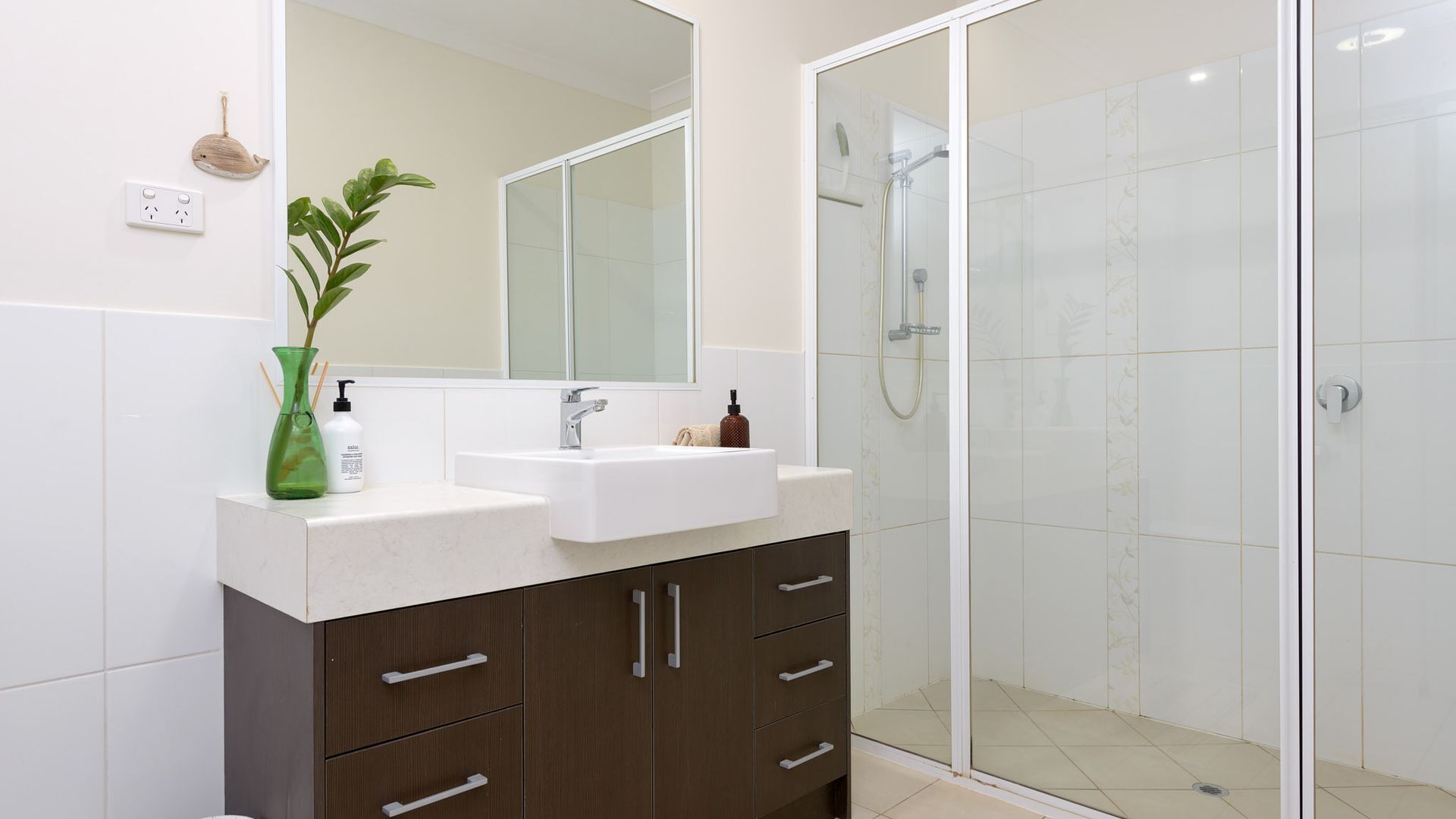 A modern bathroom with a white sink, dark wooden cabinets, a large mirror, and a glass shower enclosure.