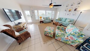 A living room with a TV, two sofas, a coffee table, and a patterned ottoman. - Family Friendly, Easy Beach Access Across the Street! (St. George Island)