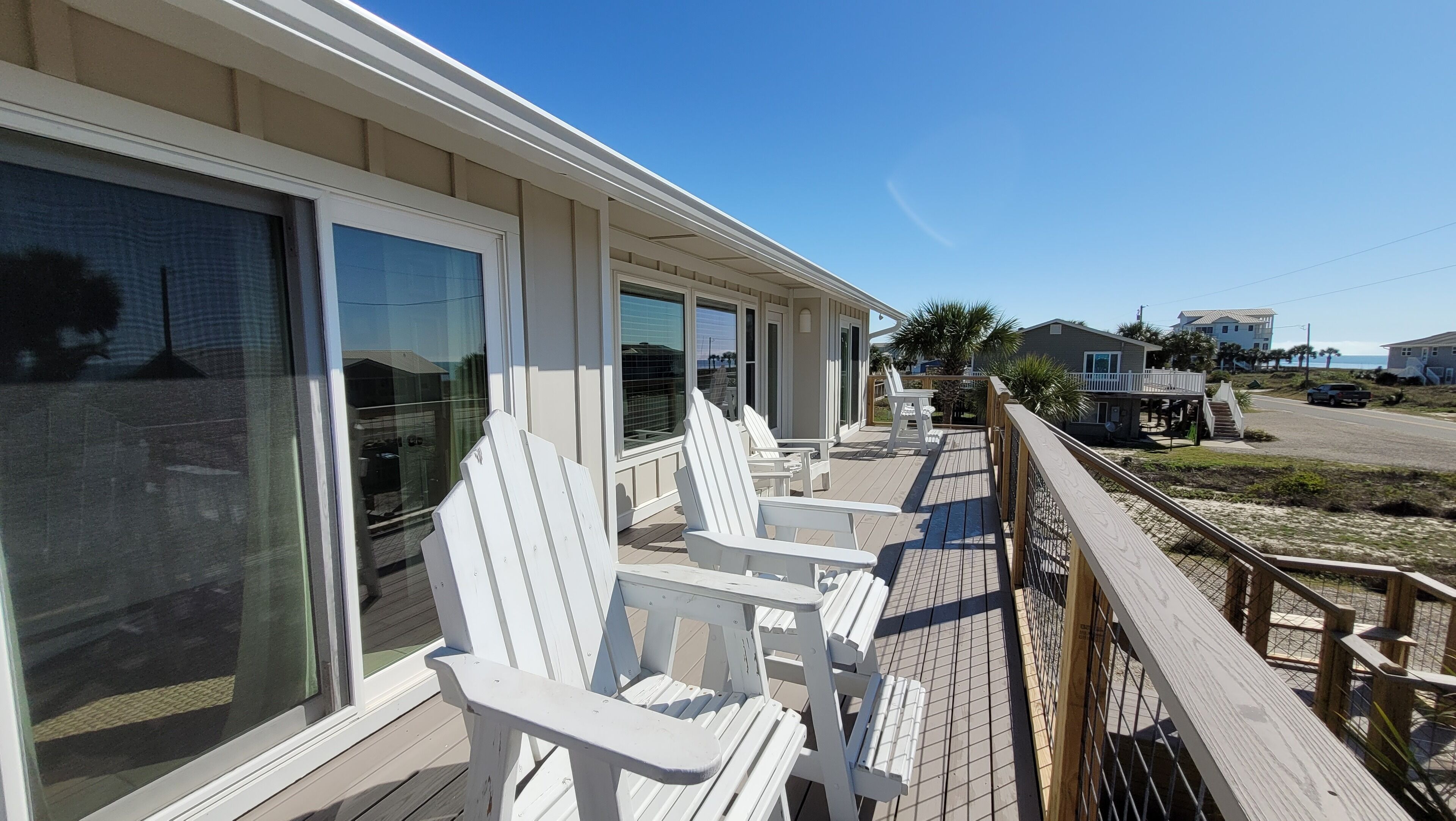 A beachfront property with a covered deck, white Adirondack chairs, and a view of the ocean.