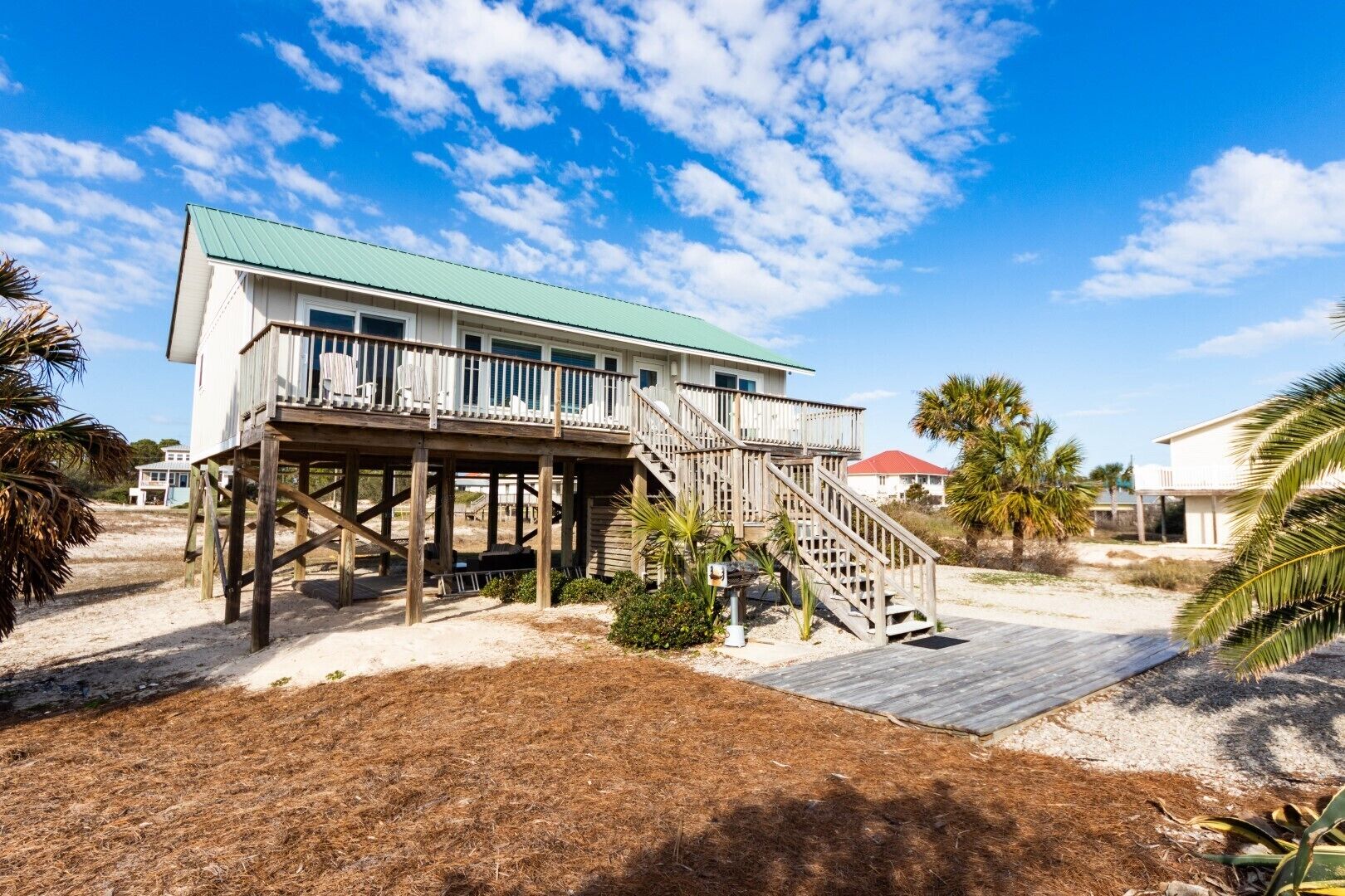 Una casa sulla spiaggia con una veranda in legno e una scala che conduce a un balcone.