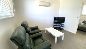 Een woonkamer met een groene bank, een witte salontafel en een televisie op een dressoir.
