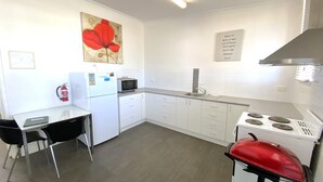 Een kleine keuken met witte kastjes, een magnetron, een gasfornuis en een rode grill.