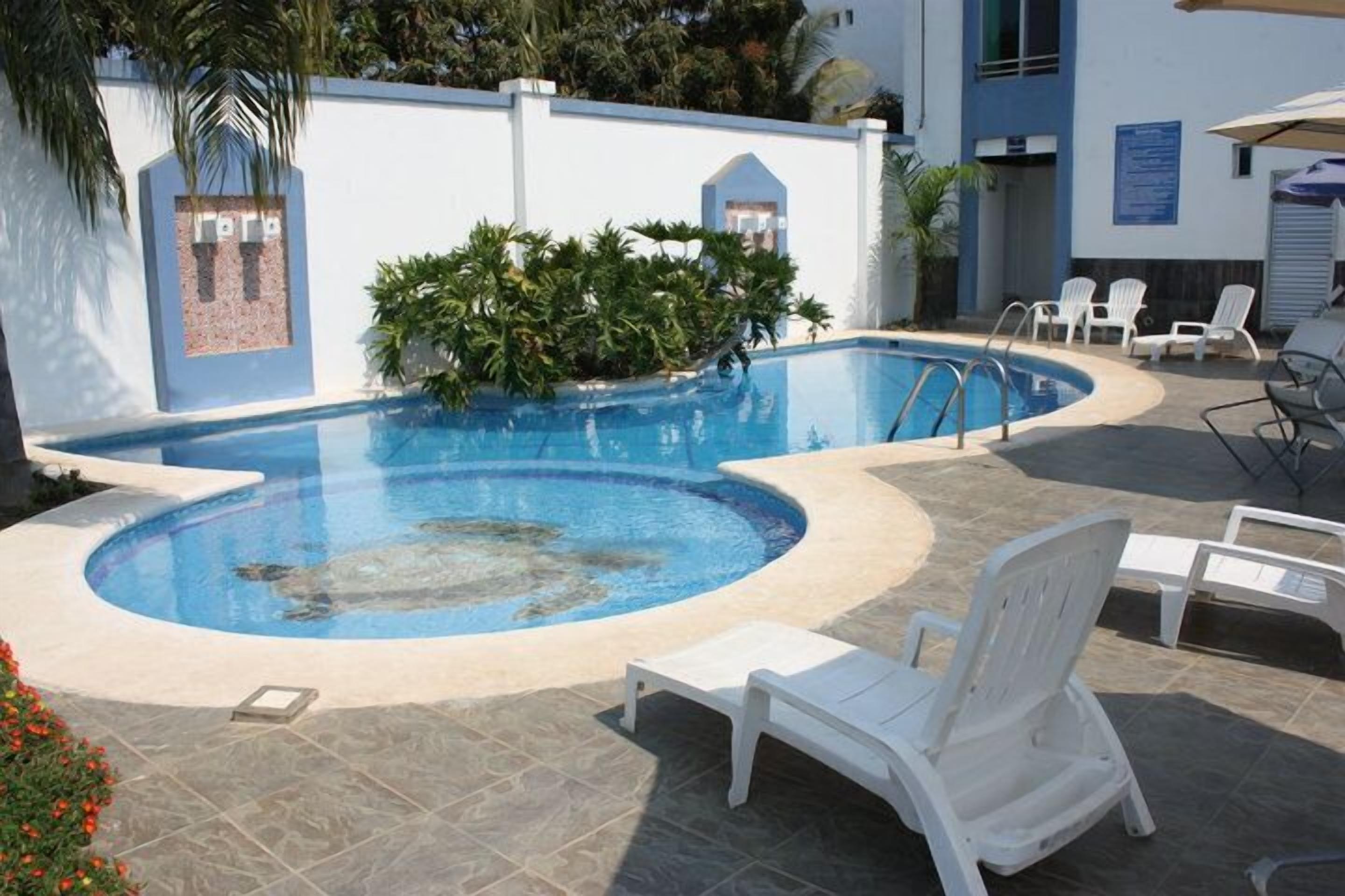 A swimming pool with a hot tub, surrounded by white lounge chairs and a tiled deck.