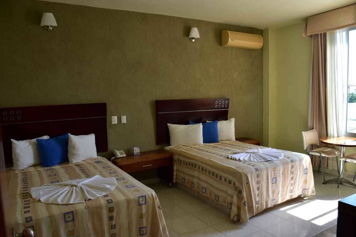 A hotel room with two beds, a small table, and a chair.