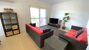 A living room with a sofa, a television, and a potted plant. - Osprey Holiday Village Unit 104  - Villa with a Pool in the Complex (EXMOUTH)