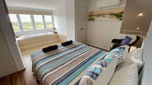 A bedroom with a large bed, a bathroom with a bathtub, and a view of the outdoors. - Osprey Holiday Village Unit 104  - Villa with a Pool in the Complex (EXMOUTH)