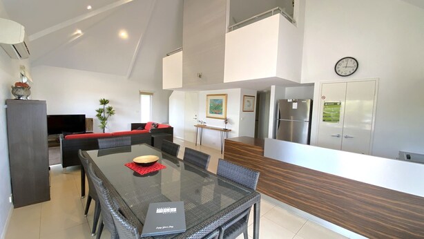 A modern kitchen with a dining area, featuring a glass-top table, wicker chairs, and a built-in refrigerator. - Osprey Holiday Village Unit 104  - Villa with a Pool in the Complex (EXMOUTH)