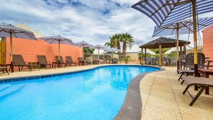 A swimming pool with lounge chairs and umbrellas, surrounded by a brick wall and palm trees. - Osprey Holiday Village Unit 104  - Villa with a Pool in the Complex (EXMOUTH)