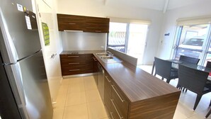 A modern kitchen with dark wooden cabinets, a stainless steel sink, and a dining area with black chairs. - Osprey Holiday Village Unit 104  - Villa with a Pool in the Complex (EXMOUTH)
