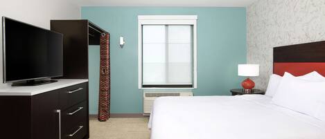 A hotel room with a bed, a TV on a dresser, a window, and a nightstand with a lamp.