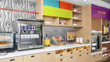 Zona de desayuno autoservicio con vitrinas refrigeradas, una máquina de café y diversos recipientes de comida.