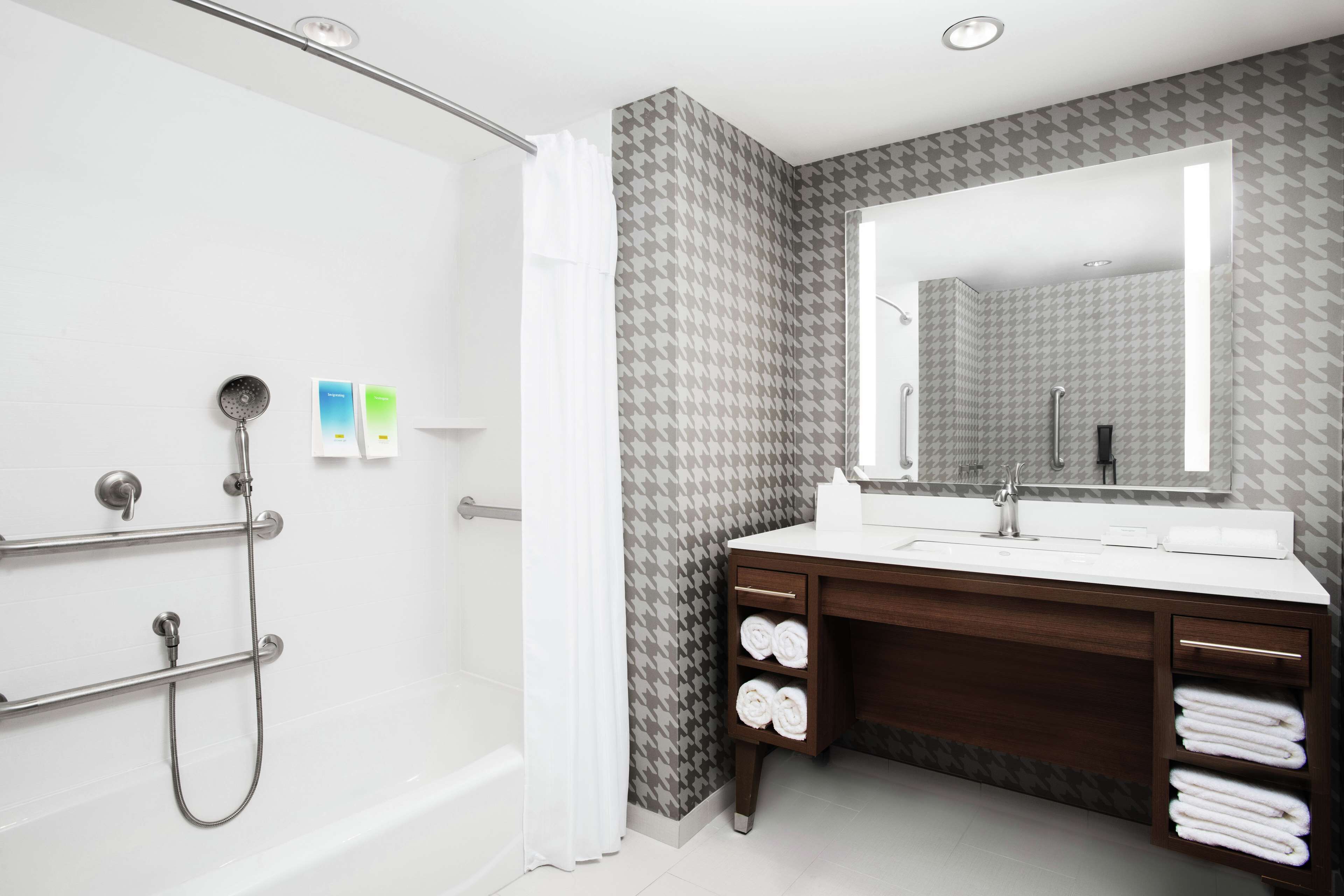 Un baño moderno con ducha, tocador con espejo y perchero.